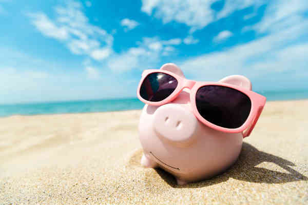 a piggy bank with sunglasses chilling on a beach