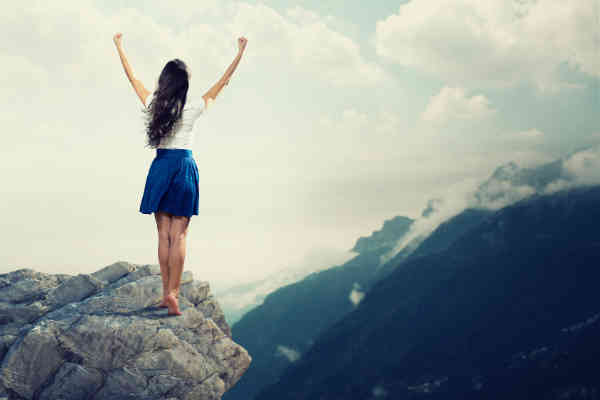 woman has her hands in the air on mountaintop